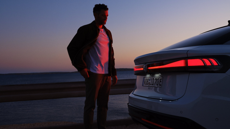 Ein Mann steht am Heck eines VW ID.7 im Dunkeln und wird von den Rückleuchten rot angeleuchtet.