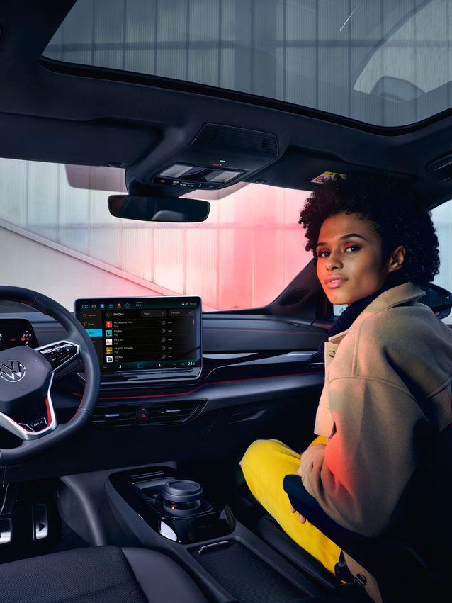 VW ID.4 GTX Innenraum mit Blick auf die Vordersitze und Cockpit. Frau sitzt auf Beifahrersitz mit Blick nach hinten.