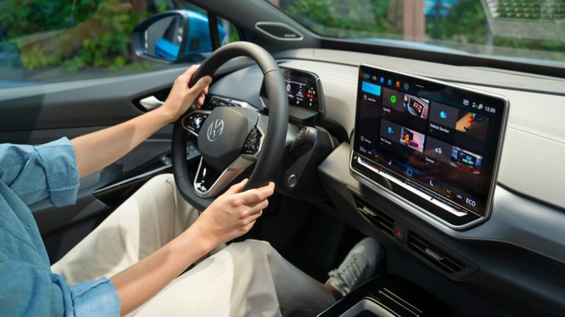 Ansicht des VW ID.4 Interieur. Schräger Seitenblick auf das Multifunktionslenkrad und Infotainmentsystem. Auf dem Fahrersitz sitzt eine Person, die das Fahrzeug lenkt. 
