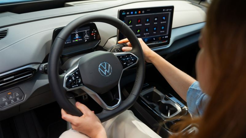 Vue intérieure d’une Volkswagen ID.4 à l’arrêt. Une femme est assise sur le siège conducteur, sa main droite actionne le levier de vitesses du volant.