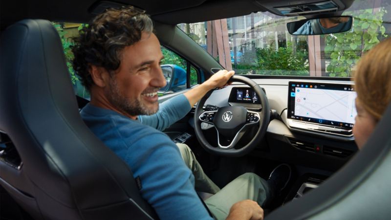Un uomo seduto sul sedile del conducente di una Volkswagen ID.4 parcheggiata sorride a una donna seduta sul sedile del passeggero anteriore. Foto scattata dal sedile posteriore destro.