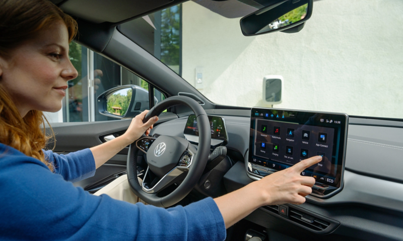 Une femme rousse, assise dans le siège du conducteur d'une VW ID.4 à l'arrêt, utilise le système d'infodivertissement. 