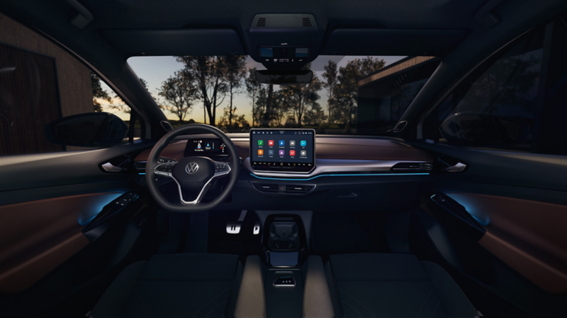 Innenansicht eines VW ID.5 bei Dunkelheit, Blick von der vorderen Mittelarmlehne auf das Lenkrad, das Infotainment-Display und die pink beleuchtete Instrumententafel. Das Display zeigt die Einstellungen der Ambientebeleuchtung. 