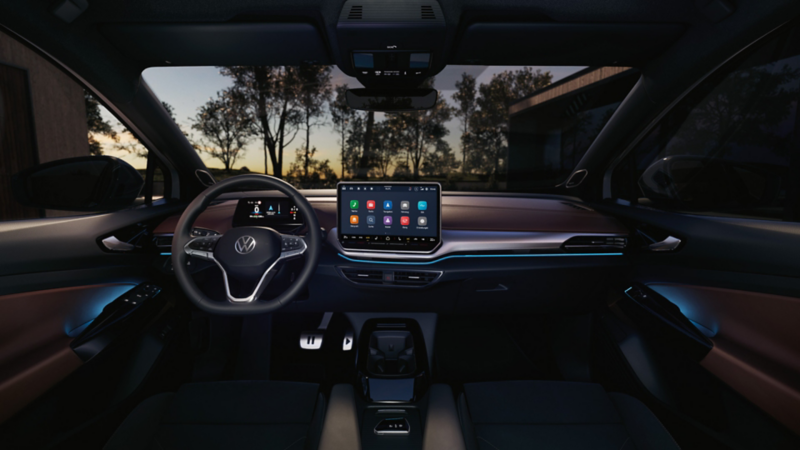 Innenansicht eines VW ID.5 bei Dunkelheit, Blick von der vorderen Mittelarmlehne auf das Lenkrad, das Infotainment-Display und die pink beleuchtete Instrumententafel. Das Display zeigt die Einstellungen der Ambientebeleuchtung. 