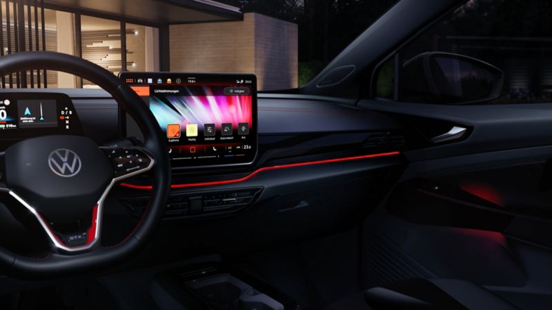 Innenraum von einem roten VW ID.5 GTX bei Dunkelheit. Blick auf das Lenkrad, das Infotainment-Display und die rot beleuchtete Instrumententafel. 