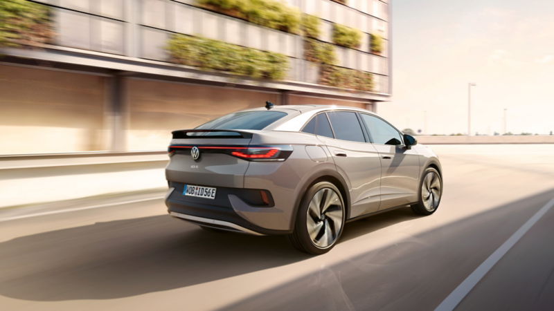Ein grauer VW ID.5 fährt auf einer Straße an einem begrünten Gebäude vorbei.