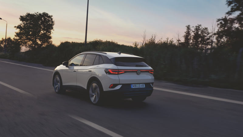 Un VW ID.4 blanc, roule sur une route, vu de l'arrière.
