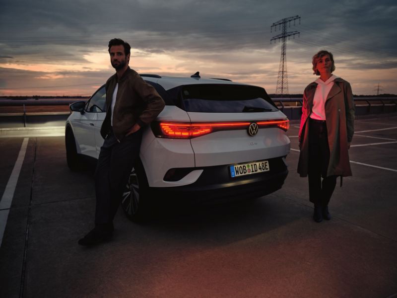 Weißer VW ID.4 steht auf Parkplatz im Dunkeln. Ein Mann und eine Frau stehen am Heck.
