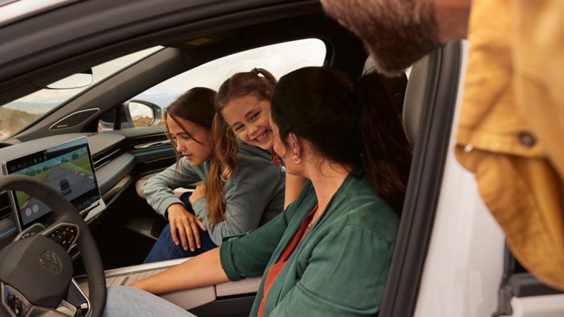 Une famille est assise à bord de la VW ID.7 et l’une des filles regarde l’écran du système d’info-divertissement sur lequel se déroule un match. 