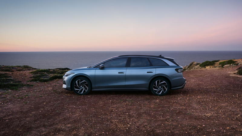 Ein blauer VW ID.7 Tourer steht oben auf einer Klippe im Sonnenuntergang, dahinter das Meer.
