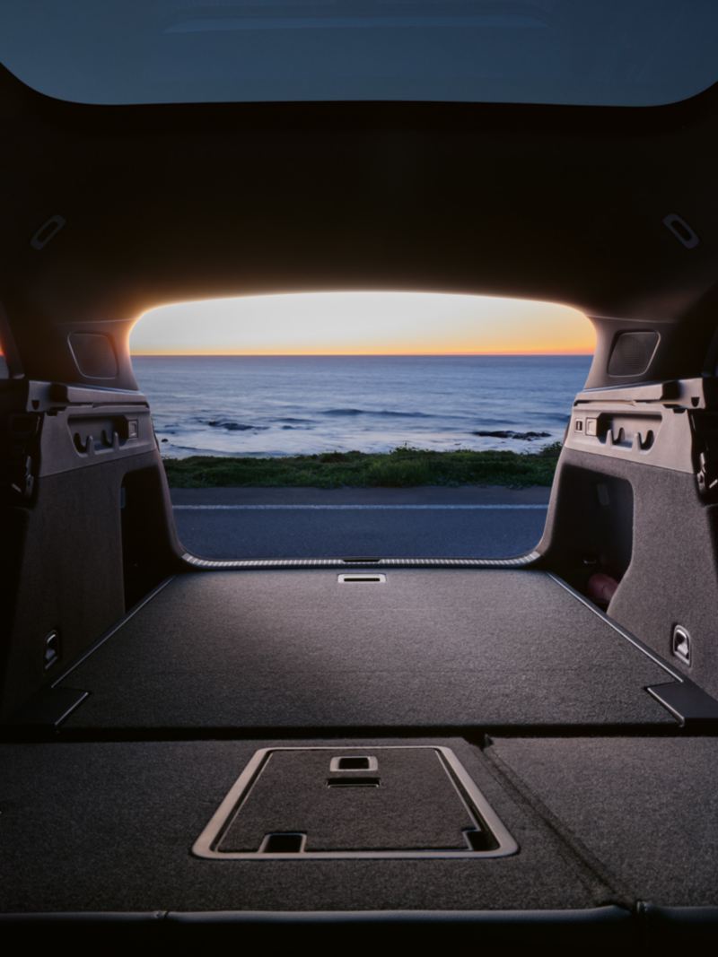 the inside of an ID.7 Tourer with the boot open looking out onto the ocean over an orange sunset