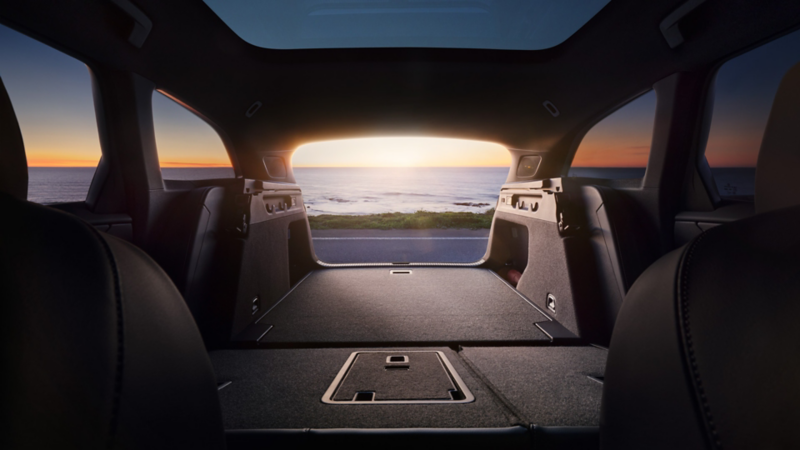 Innenansicht des Kofferraums eines VW ID.7 Tourer mit umgeklappten Rücksitzen, durch die offene Heckklappe ist das Meer sichtbar.