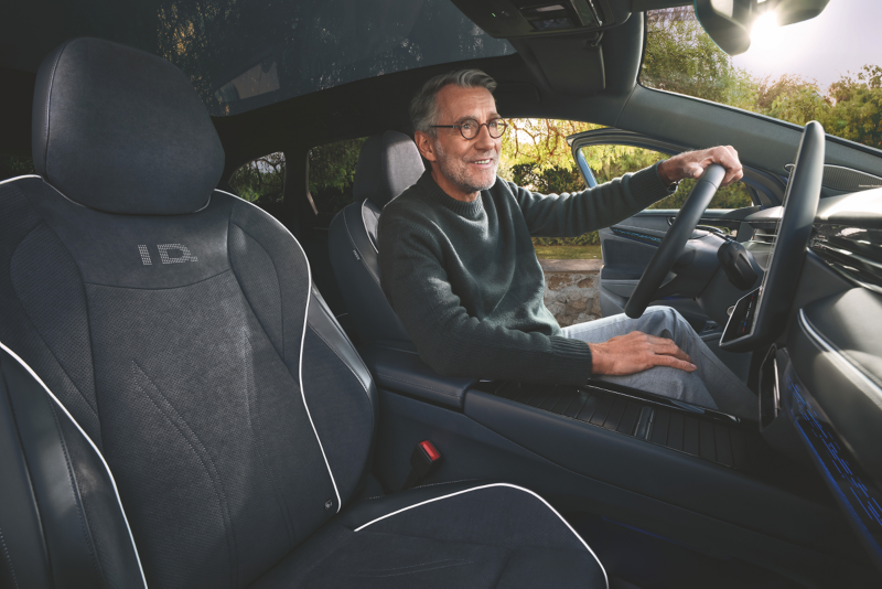 Interieur shot van de Volkswagen ID.7 Tourer, focus ligt op de voorstoelen waarbij een man achter het stuur zit dit glimlacht