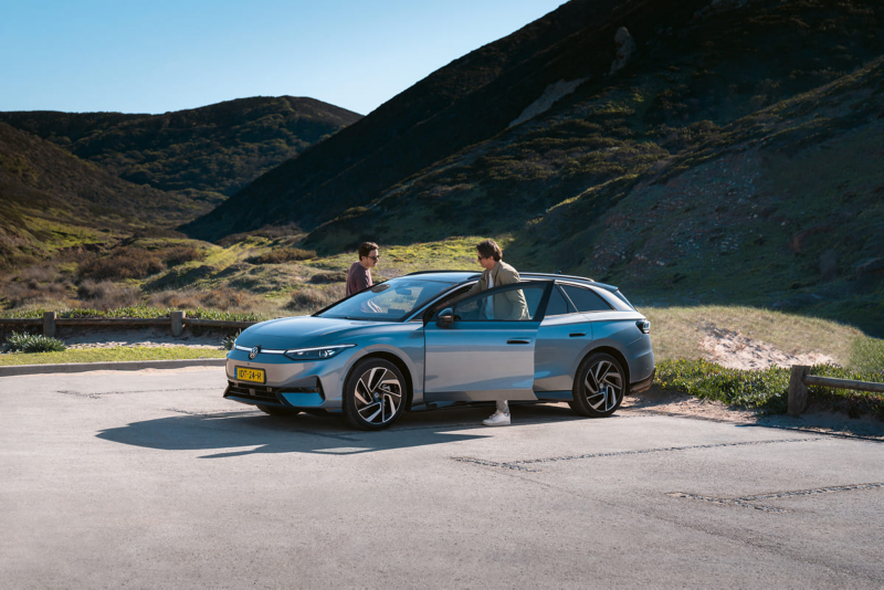 Twee mannen stappen in een Volkswagen ID.7 Tourer die geparkeerd staat op parkeerplaats in een afgelegen bergachtig gebied