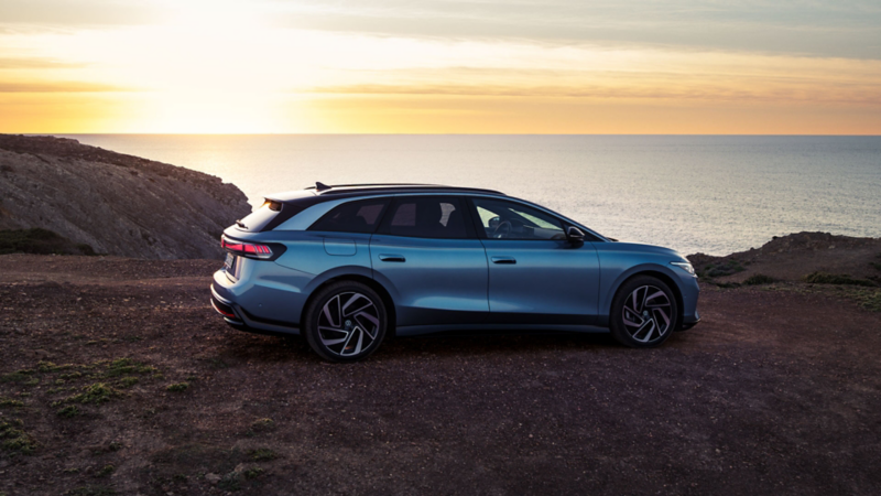 Ein blauer VW ID.7 Tourer steht oben auf einer Klippe im Sonnenuntergang, dahinter das Meer.