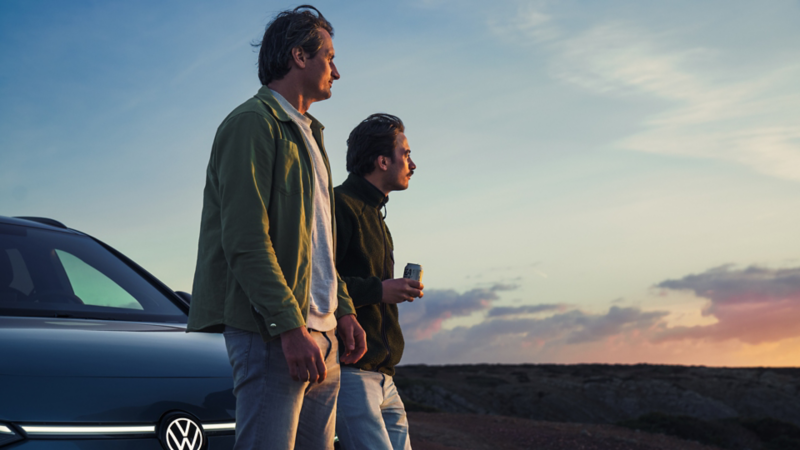 two men outside looking out into the distance. an ID.7 Tourer is parked behind them