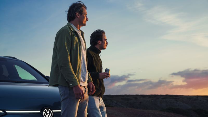 Deux hommes contemplent un coucher de soleil devant une VW ID.7 Tourer.