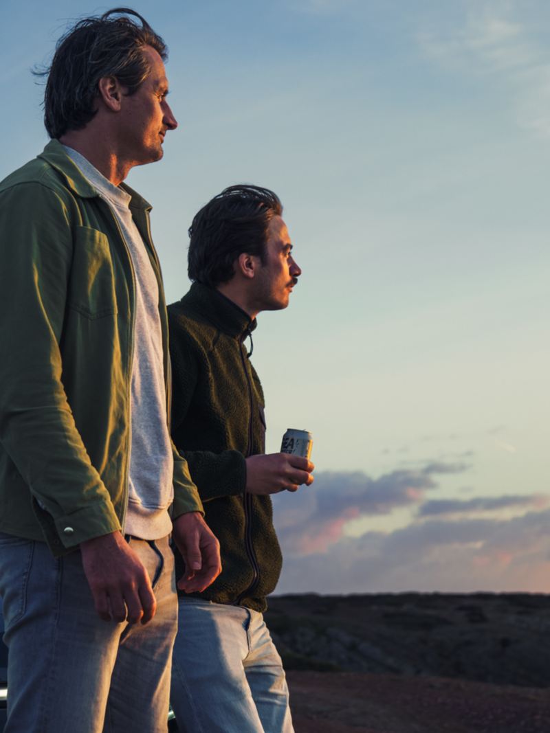 Zwei Männer stehen vor einem ID.7 Tourer und genießen den Sonnenuntergang
