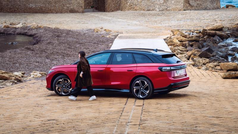 Vista di una Volkswagen ID.7 GTX Tourer rossa. Una donna cammina lungo l’auto