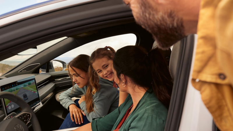 To barn og en kvinne ser på infotainmentsystemet i en Volkswagen ID.7. Faren seg gjennom førerdøren.