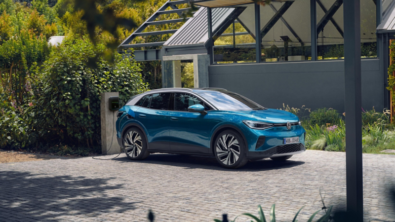 Ein blauer VW ID.4 parkt seitlich vor einem modernen Haus und lädt an einer Wallbox.