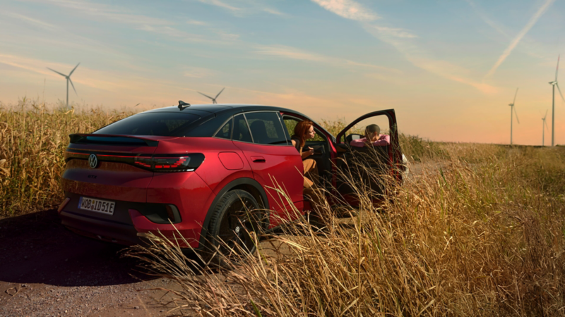 Ein roter VW ID.5 GTX steht auf einem Feldweg. Eine Frau steigt aus, ein Mann lehnt an der geöffneten Beifahrertür.