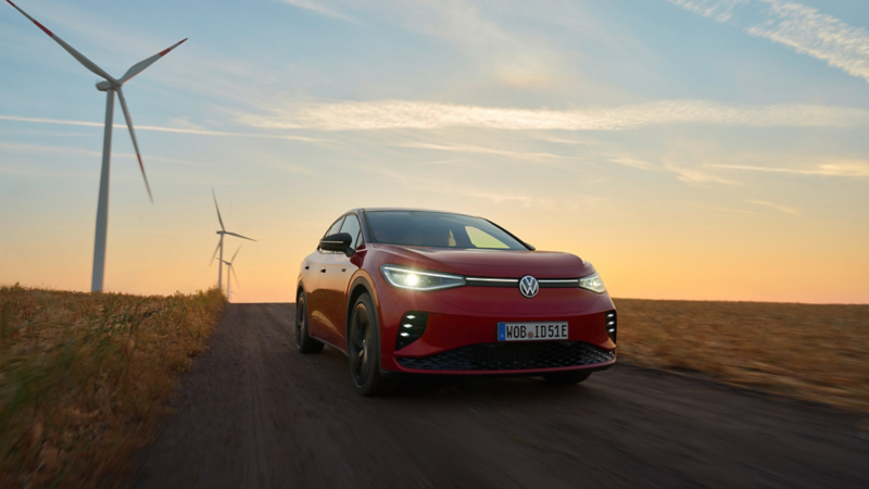 Ein roter VW ID.5 GTX fährt auf einer Landstraße mit Windrädern im Hintergrund.