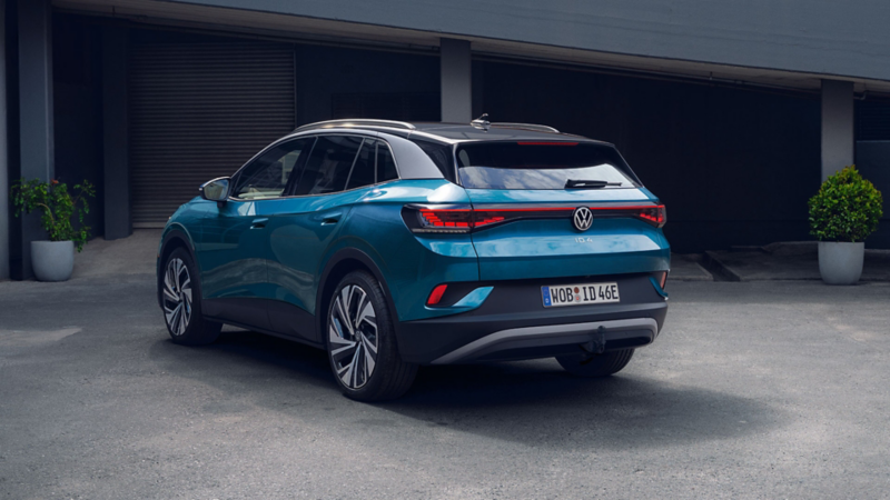  Vue de l'intérieur d'une Volkswagen ID.4, montrant le tableau de bord, le volant et les écrans numériques. Le volant est doté du logo VW et le tableau de bord présente un éclairage d'ambiance bleu vif. Au centre, l'écran d'infodivertissement affiche une carte.