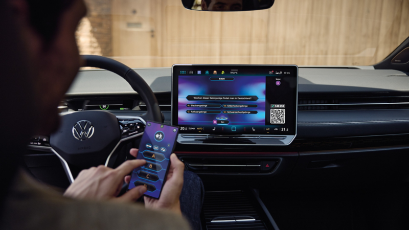Ein Mann spielt im VW ID.7 Tourer per In-Car-App ein Quiz am Smartphone.