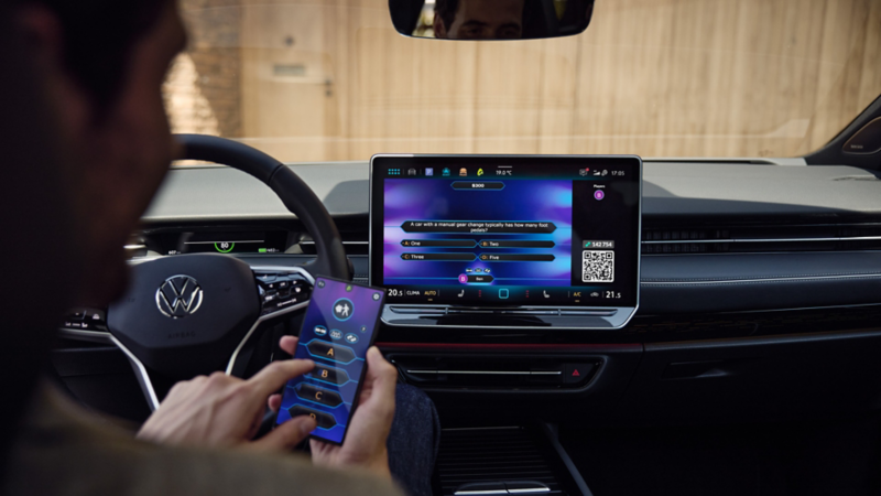 Mężczyzna gra w quiz na smartfonie, korzystając z aplikacji In-Car w VW ID.7 Tourer.