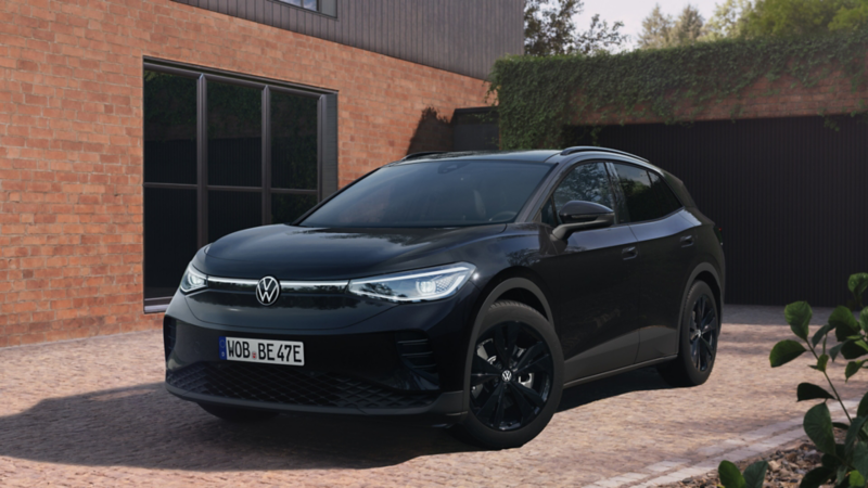Ein schwarzer ID.4 BLACK EDITION steht in einer Hofeinfahrt eines roten Hauses mit Garage. Die Garage ist mit Efeu bewachsen.