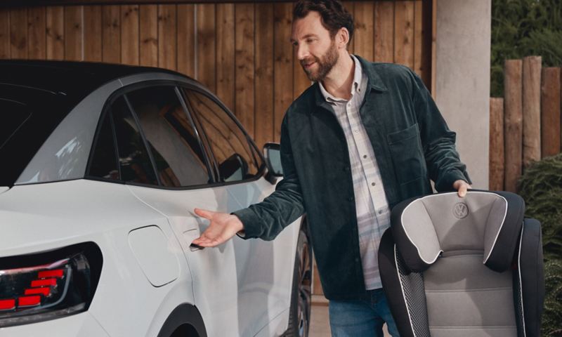 A man holding a Volkswagen Genuine child seat opens the rear door of a VW ID.5.