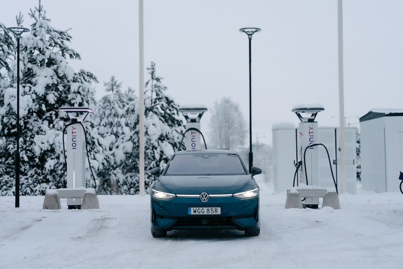 En mörkblå VW ID.7 står parkerad vid en laddstation i vinterlandskap