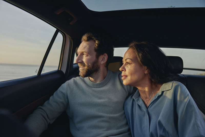 A couple sat inside car looking out the window at the ocean
