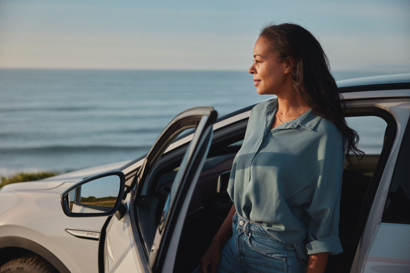 Woman standing at car side door looking out at ocean