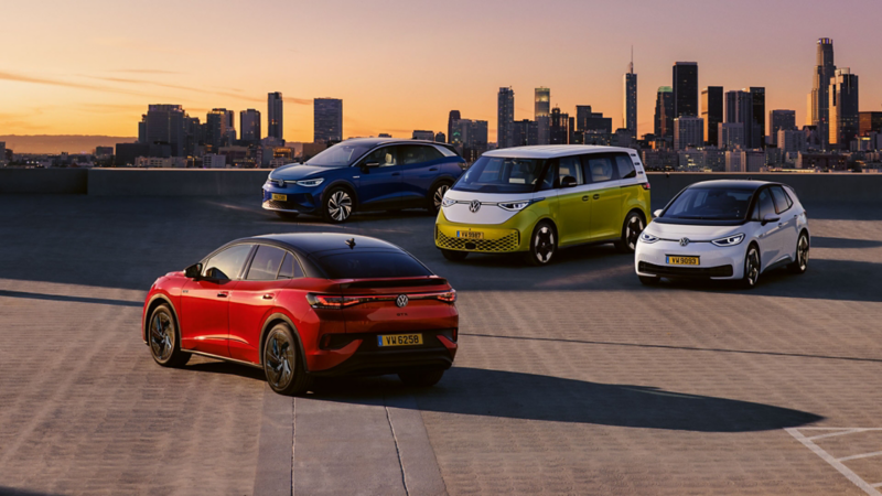 Quatre véhicules VW sont garés sur un parking au coucher du soleil.