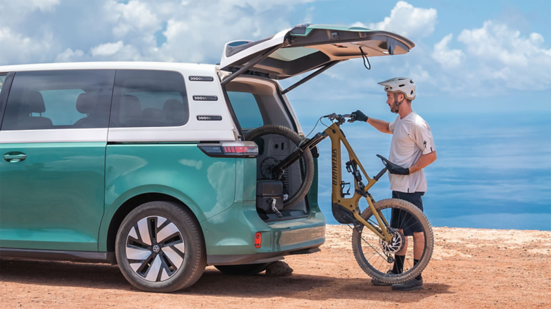 Un VW ID. Buzz con el maletero abierto y un hombre introduciendo una bicicleta.