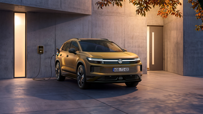Ein oliv-bronzefarbener VW ID.Tiguan steht vor einem Haus in der Abenddämmerung an einer Wallbox.