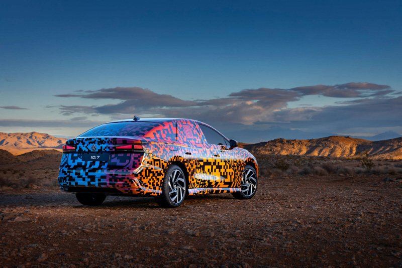 Volkswagen ID.7 in vibrant camouflage wrap parked in a desert landscape during golden hour, with dramatic mountains and clouds in the background.