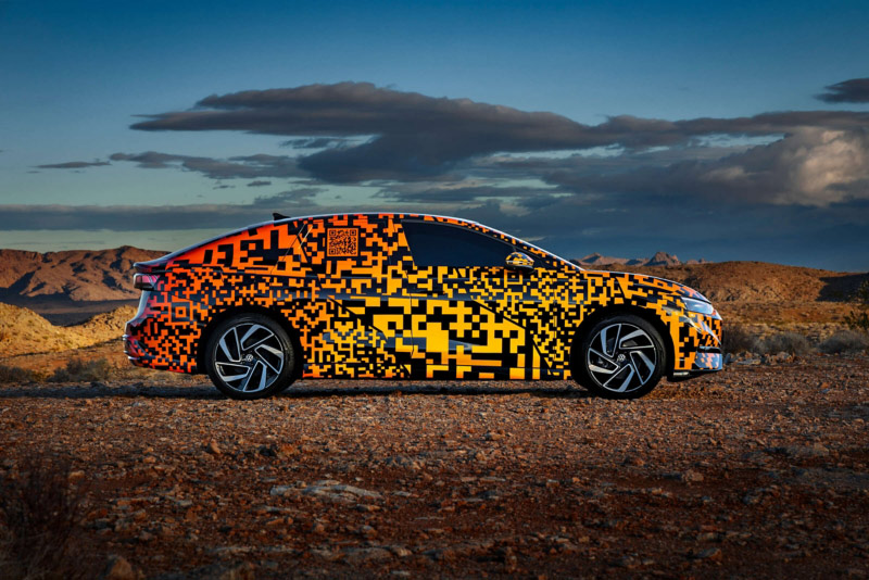 Volkswagen ID.7 exterior side view in vibrant orange camouflage wrap parked in the outback with dramatic mountains and clouds in the background.
