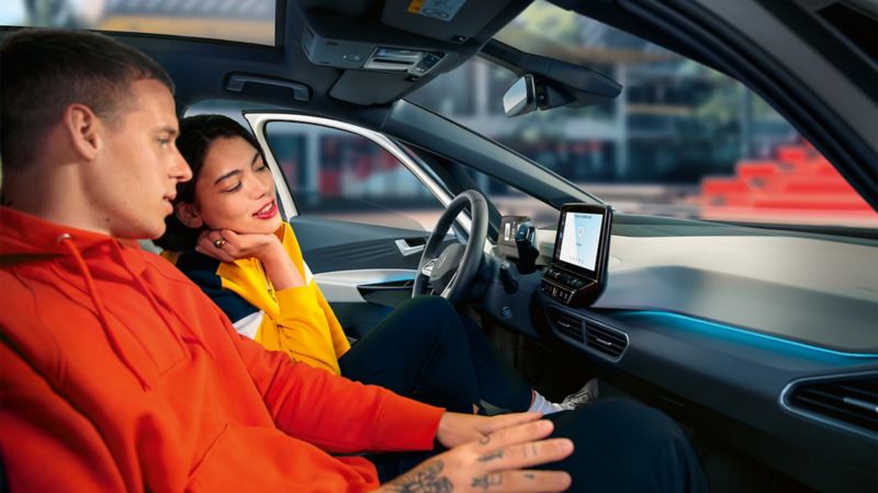 Paar im Cockpit des VW ID.3 nutzt die Sprachsteuerung und schaut auf das Infotainment-System. We Connect Start.