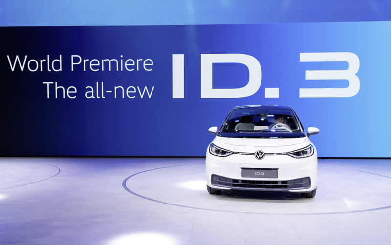 En vit Volkswagen ID.3 visas framifrån på en scen vid en världspremiär, med texten "World Premiere The all-new ID.3 i bakgrunden.