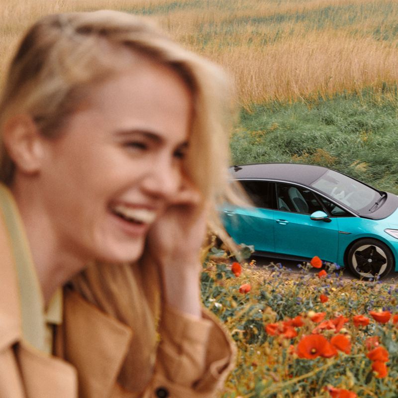 Ein türkiser VW ID.3 ist hinter einer blonden, lachenden Frau zu sehen.