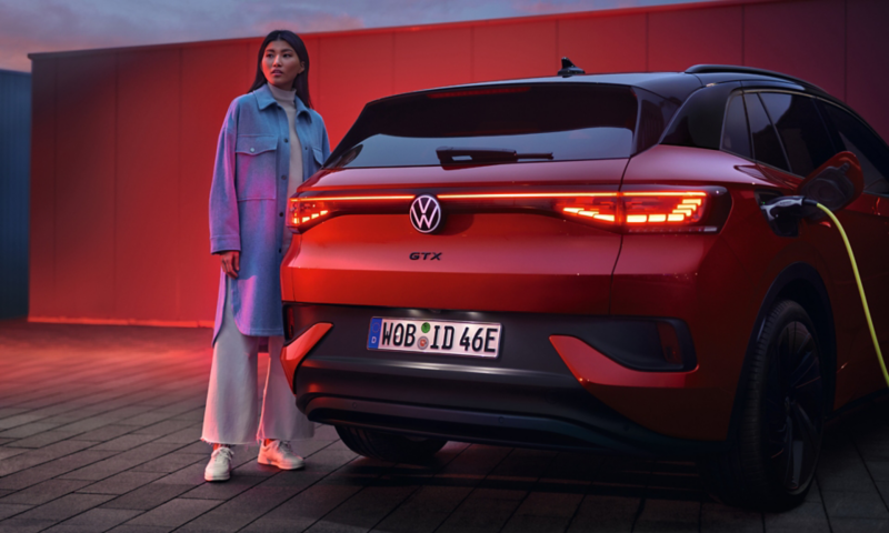 VW ID.4 GTX in red from behind while charging. Woman standing next to it.