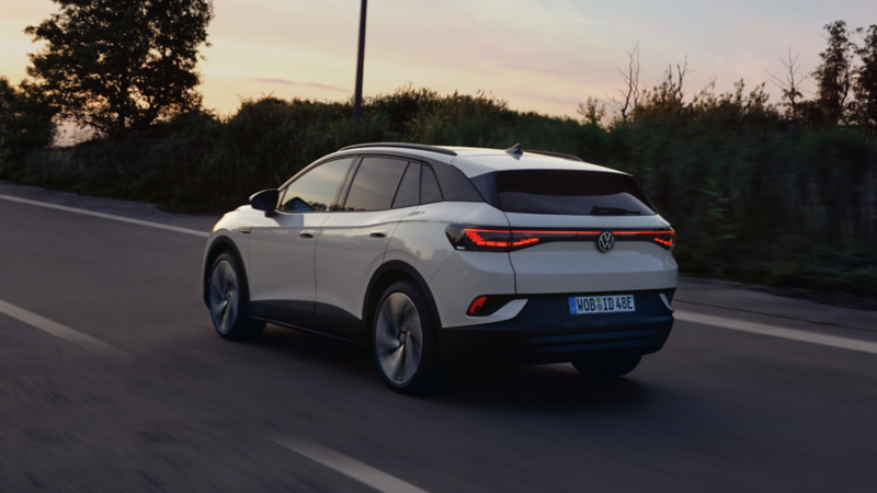 Rear view of a Volkswagen ID.4 driving on an open road, showcasing its electric SUV design and LED rear lights
