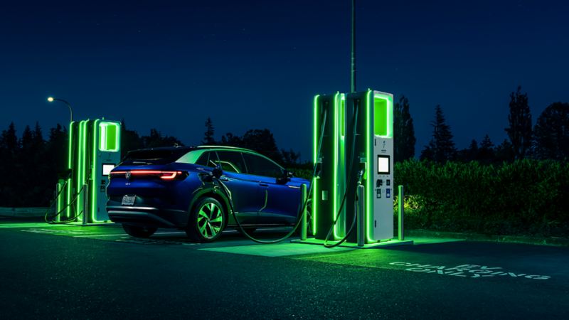 A blue ID.4 at night plugged into an electric charging station that is coloured neon green. 
