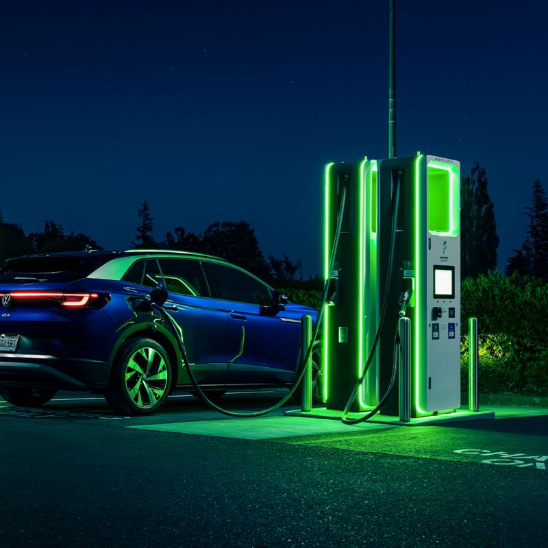 A blue ID.4 at night plugged into an electric charging station that is coloured neon green. 
