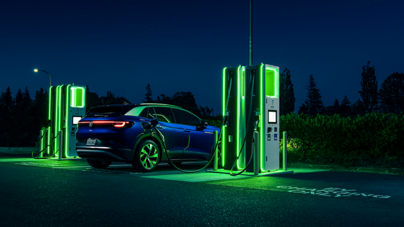 A blue ID.4 at night plugged into an electric charging station that is coloured neon green. 