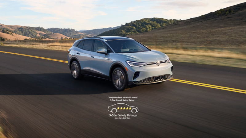 Un VUS électrique Volkswagen ID.4 gris clair, roulant sur une route panoramique avec des collines vallonnées en arrière-plan.