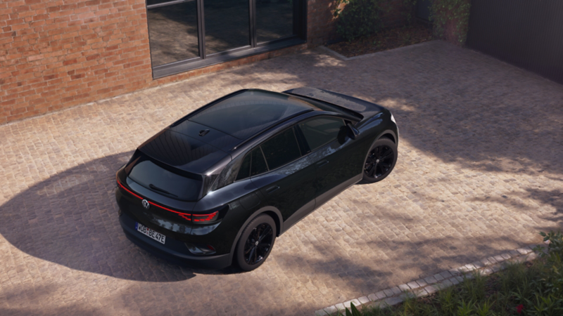 Ansicht aus der schräg linken Vogelperspektive auf einen schwarzen VW ID.4 Black Edition vor einem modernen Haus.